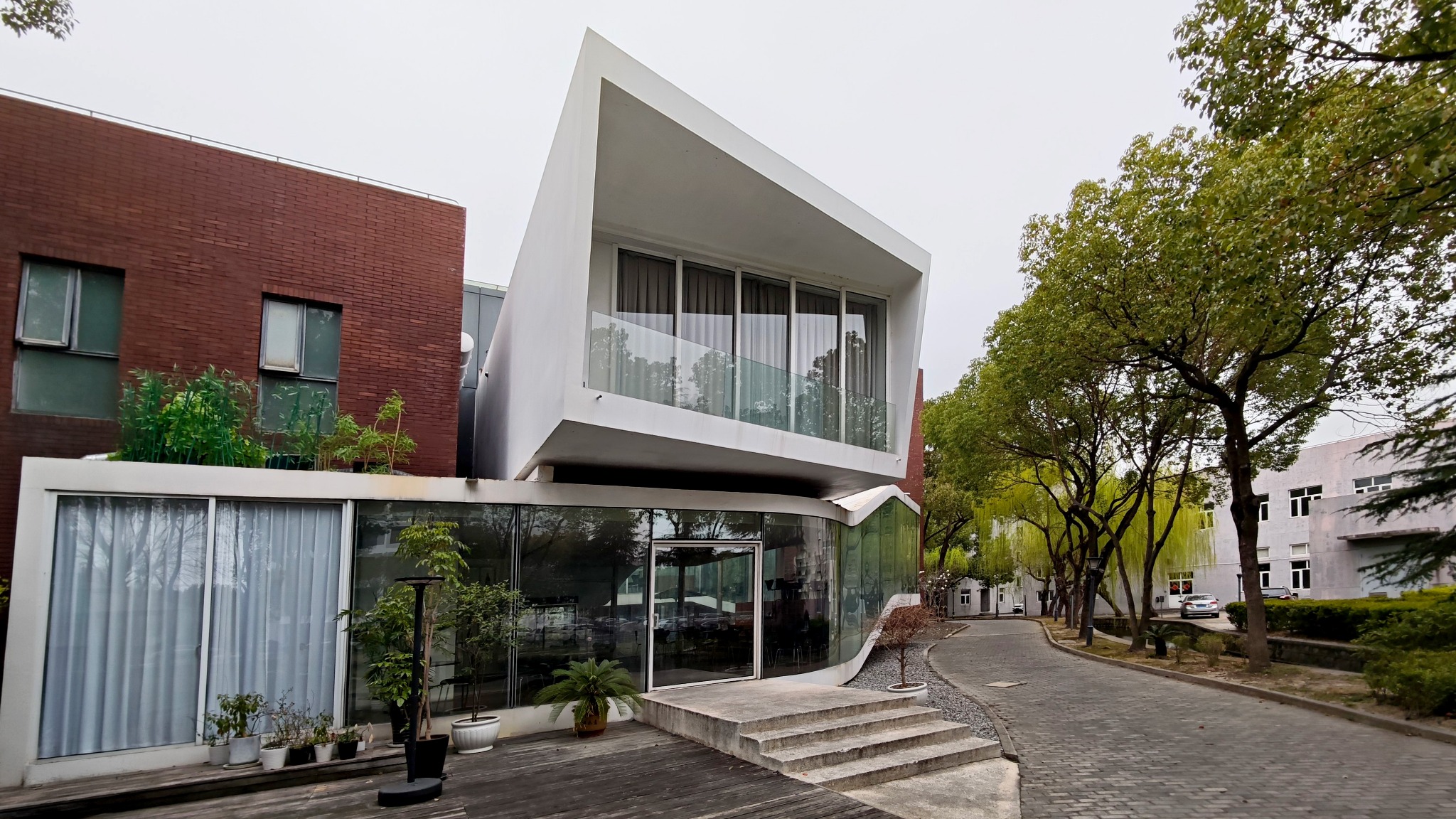 RIBO Central Club entrance with a projecting white upper room beside the tree-lined campus path