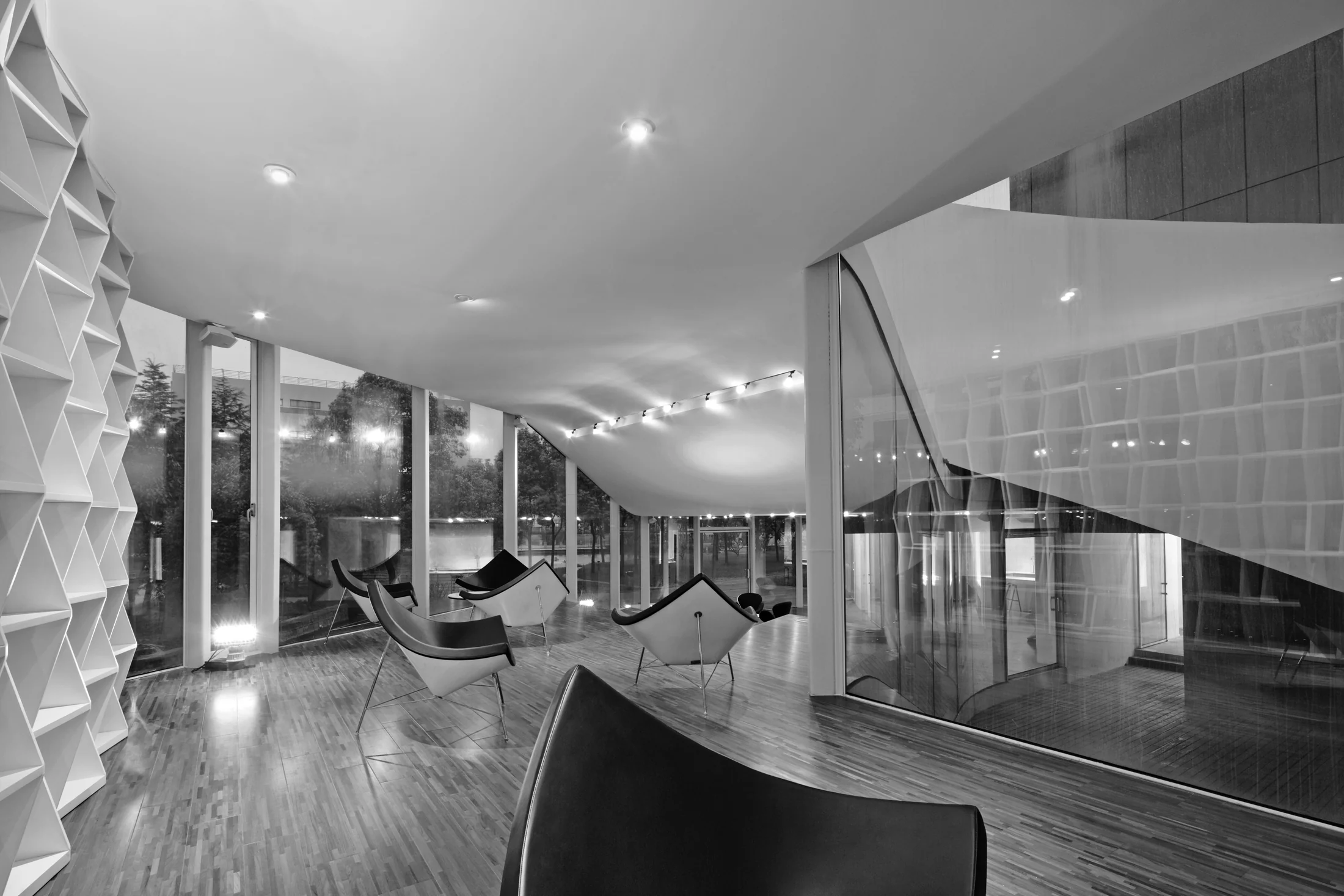 The reading lounge combines curved glazing, a continuous timber floor, and a full-height shelving wall.